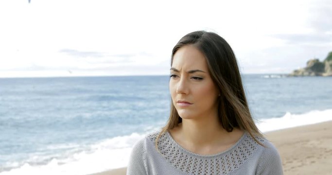 Melancholic woman walking alone on the beach looking at side