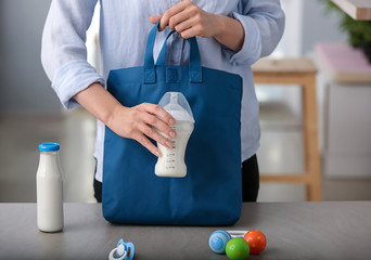 Woman putting feeding bottle of baby formula into bag at table