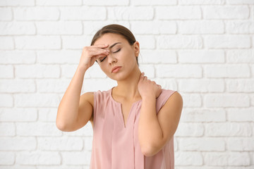 Woman suffering from headache against white brick wall