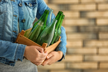 Woman holding wooden box with empty glass bottles near brick wall