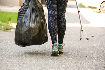 Woman with garbage bag and stick on city street