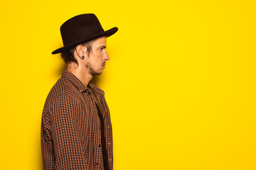 Modern and handsome guy with a black hat on a yellow background. Concept of young cool dress