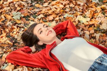 Beautiful young woman lying on fallen leaves in autumn park