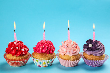 Tasty birthday cupcakes with burning candles on color background