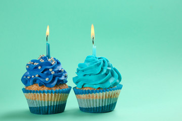 Tasty birthday cupcakes with burning candles on color background