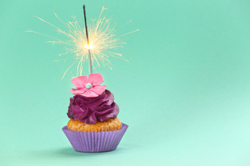 Tasty birthday cupcake with sparkler on color background
