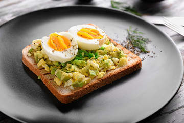 Toasted bread with cut boiled egg and avocado on plate, closeup