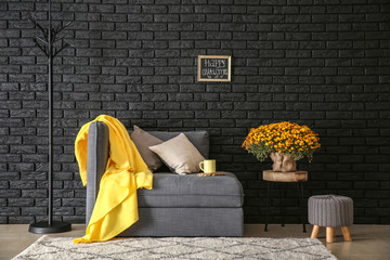 Comfortable armchair with beautiful chrysanthemum flowers near dark brick wall
