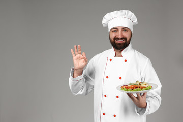 Male chef with tasty dish on grey background