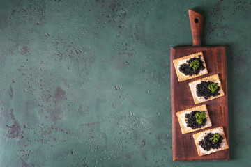 Delicious cookies with black caviar on green table