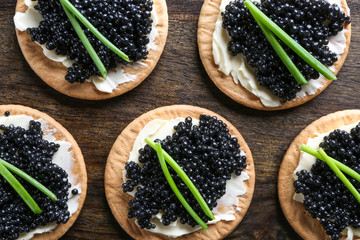 Delicious cookies with black caviar on wooden table