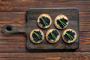 Delicious cookies with black caviar on wooden board