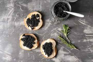 Delicious sandwiches and jar with black caviar on grey table