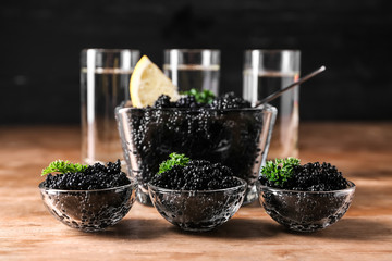 Bowls with delicious black caviar on wooden table