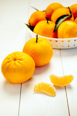 Pile of mandarins in white bowl on white wooden background