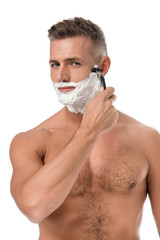 muscular shirtless man with foam on face shaving with razor isolated on white