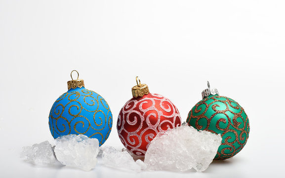 Three christmas balls decoration near stones of ice isolated on white. Winter and frost concept. Frozen pieces of ice near christmas toys. Cold weather winter season. Winter holiday concept