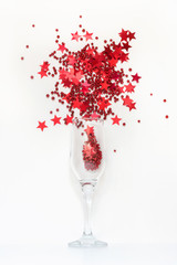 Red confetti in shape of stars poured out glasses of champagne. Top view. Christmas party. Magic night.