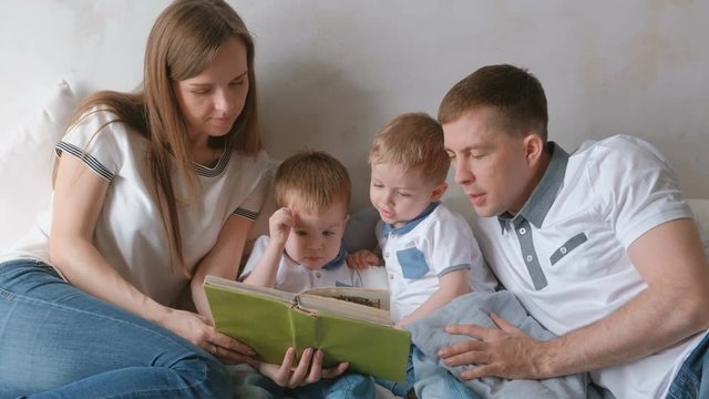 Family mom, dad and two twin brothers read books laying on the bed. Family reading time.