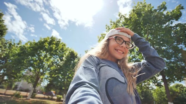 Beautiful twelve-year-old teenager girl takes a selfie with a video camera on the background of sun rays and trees
