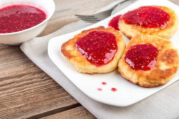 Cottage cheese pancakes, cheesecakes  with raspeberry  jam on wooden background, healthy traditional  breakfast