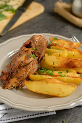 Roast pork with herbs and vegetables on rustic wooden table.