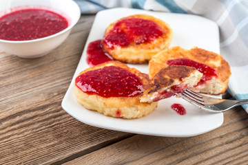 Cottage cheese pancakes, cheesecakes  with raspeberry  jam on wooden background, healthy traditional  breakfast