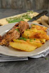 Roast pork with herbs and vegetables on rustic wooden table.