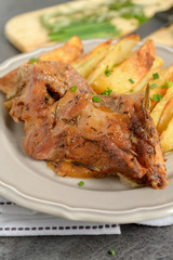Roast pork with herbs and vegetables on rustic wooden table.
