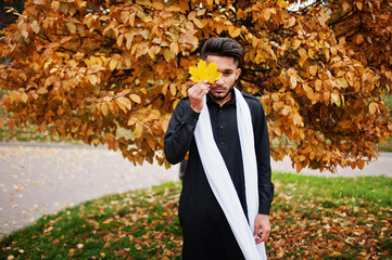 Indian stylish man in black traditional clothes with white scarf posed outdoor against yellow...