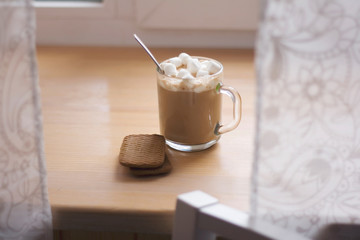 hot drink in a glass mug with cookies. cocoa with marshmellow. morning cup of coffee on the windowstill.