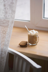 hot drink in a glass mug with cookies. cocoa with marshmellow. morning cup of coffee on the windowstill.