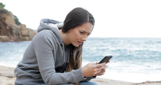Sad girl receiving bad news online on a smart phone on the beach