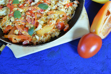 scrambled eggs with vegetables served in a pan for breakfast on dark blue background with tomatoes Bell pepper. copy space top view. omelette