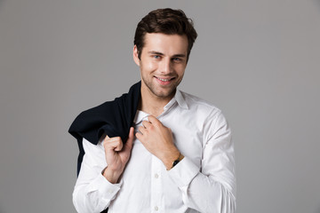 Image of positive businessman 30s smiling and holding jacket over his shoulder, isolated over gray...