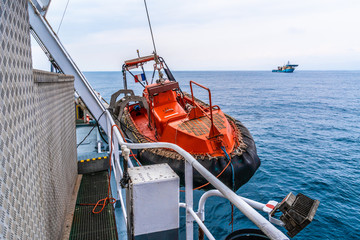 Lifeboat or FRC fast rescue craft boat in the vessel at sea. dsv diving ship is on background.