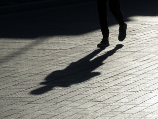 Silhouette of person walking down the street, long shadow on pavement. Man in sneakers runs on sidewalk, concept for jogging, healthy lifestyle