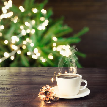 Cup of black coffee on wooden table in cafe. Christmas lights and gold garland on background.