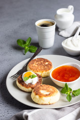 Fototapeta na wymiar Cottage cheese pancakes or fritters with jam, natural yogurt or sour cream and mint. Traditional Ukrainian and Russian cuisine. Syrniki. Healthy and diet breakfast.