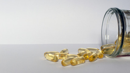 yellow pills of fish oil on a bright background with a glass jar next to it.
