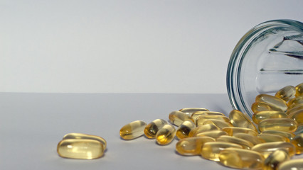 yellow pills of fish oil on a bright background with a glass jar next to it.