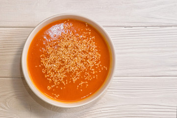 Close up, top view. White bowl with bright pumpkin cream soup, sprinkled with sesame seeds. Copy space.