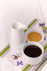 A cup of coffee, milk in a jar and honey in a bowl on a colorful napkin