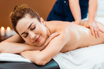 Obraz na płótnie Canvas beautiful smiling girl with closed eyes enjoying massage in spa