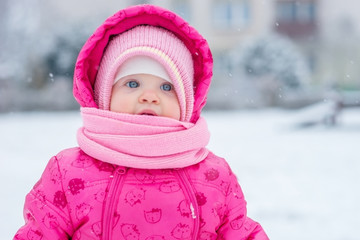 Baby in winter overalls wrapped in a scarf walks on a snow-covered street and sculpts from snow.