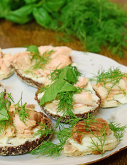 Smoked salmon canapes on white plate. Toppings:  fish, cream cheese, dill and basilica.