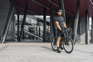 Sportsman riding bike next to modern building inside urban bridge.