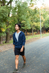 Image of pleased asian guy in casual wear and eyeglasses, walking down road through park with green...