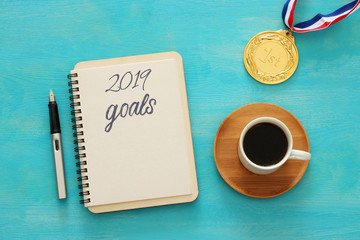 Top view 2019 goals list with notebook, cup of coffee over wooden desk.