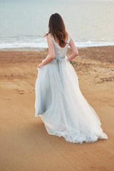 Fototapeta na wymiar Bride walking along the sea wearing a beautiful gray wedding dress